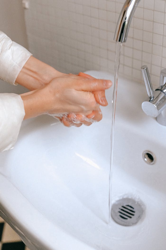 Close-up of hands being washed with water and soap in a bathroom sink, promoting hygiene.