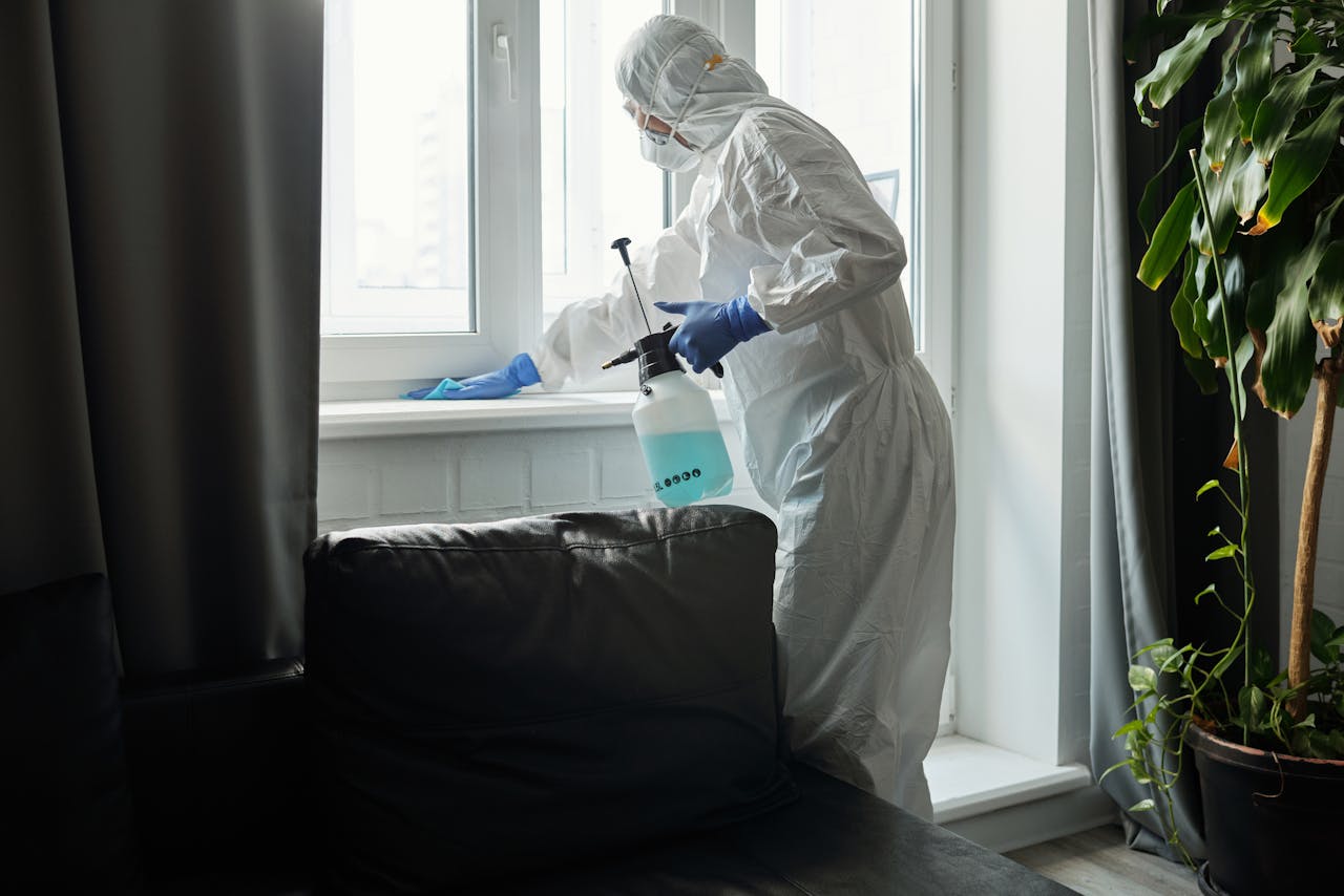 Person in PPE disinfecting indoor window area during COVID-19 pandemic.